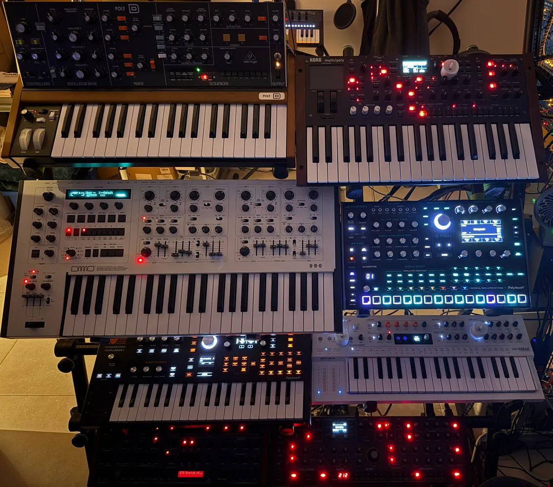 A stack of keyboards and desktop synthesisers on a stand, with lit displays and pads.