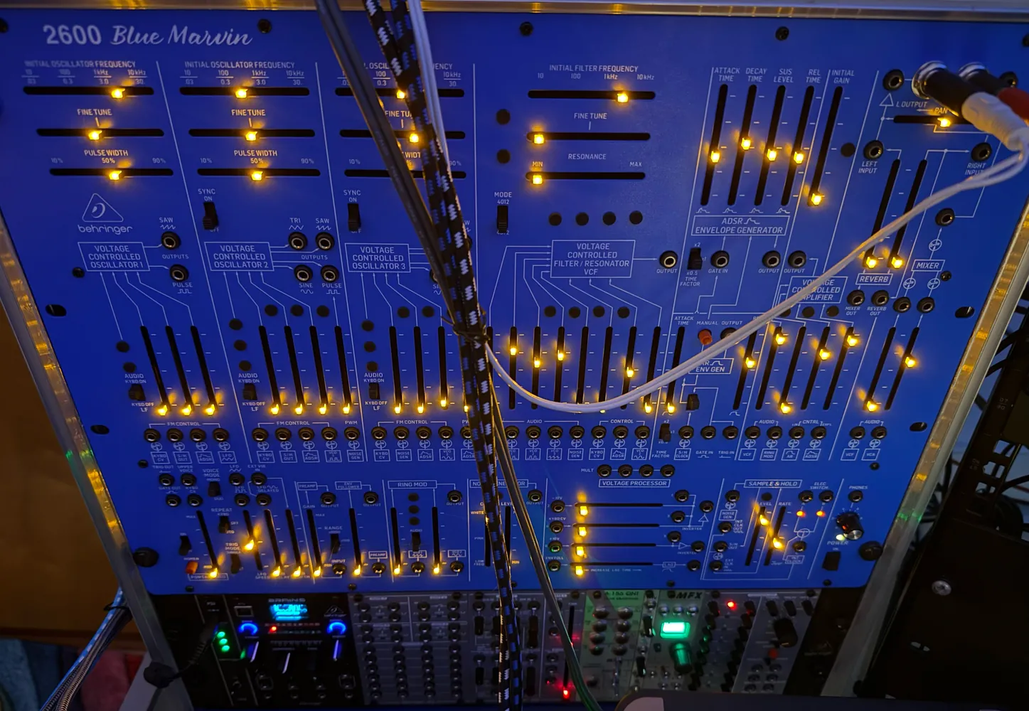 A large blue modular synthesiser panel covered in sliders lit in orange.