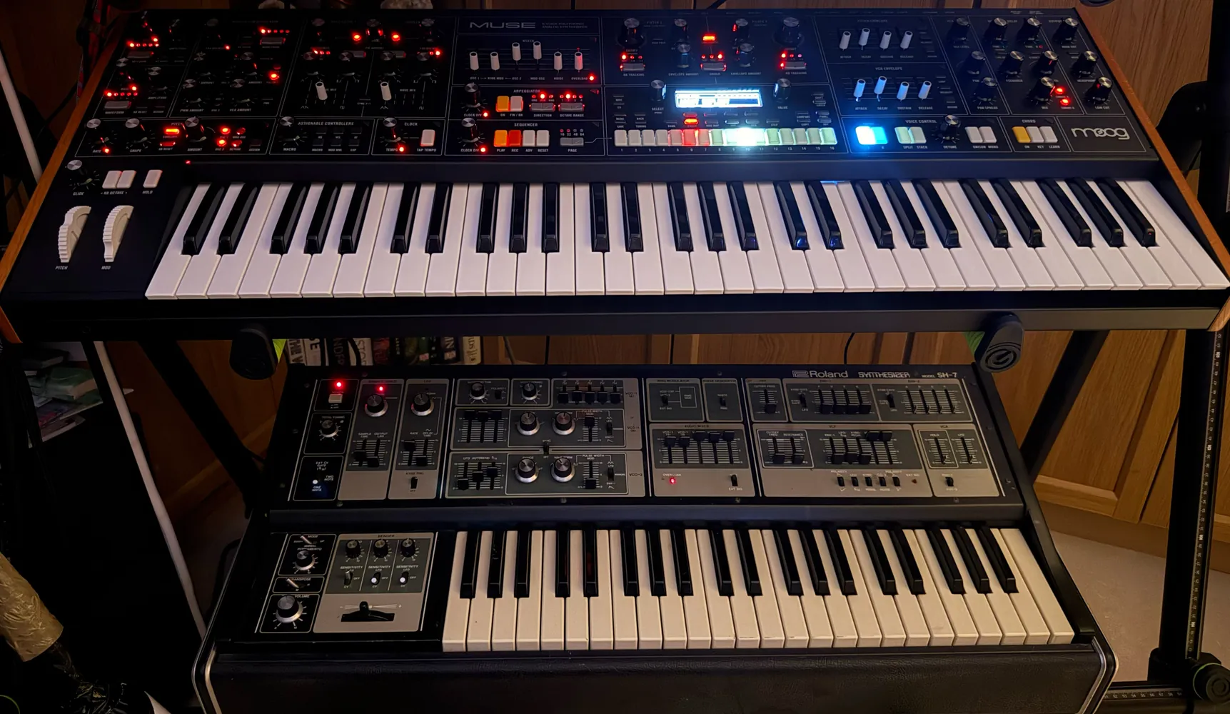 A large keyboard synthesiser with rows of lit controls, above a second keyboard on the stand below.