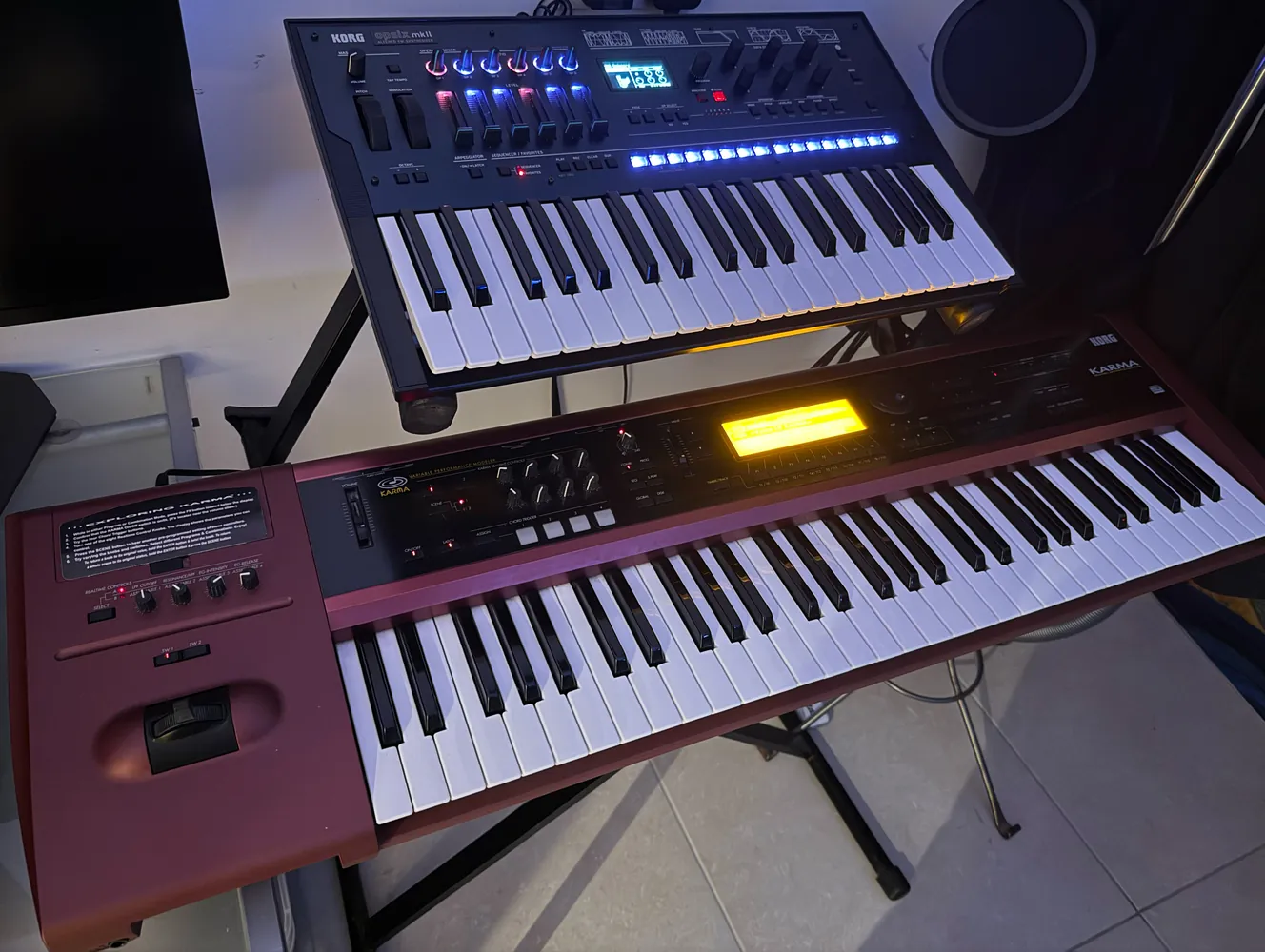 Two keyboards on a stand, one above the other, the lower one in a red wooden case with an orange display.